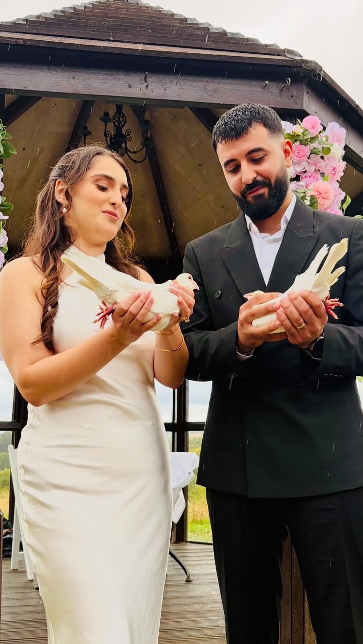 A bride and groom holding white doves in their hands under a wooden gazebo.