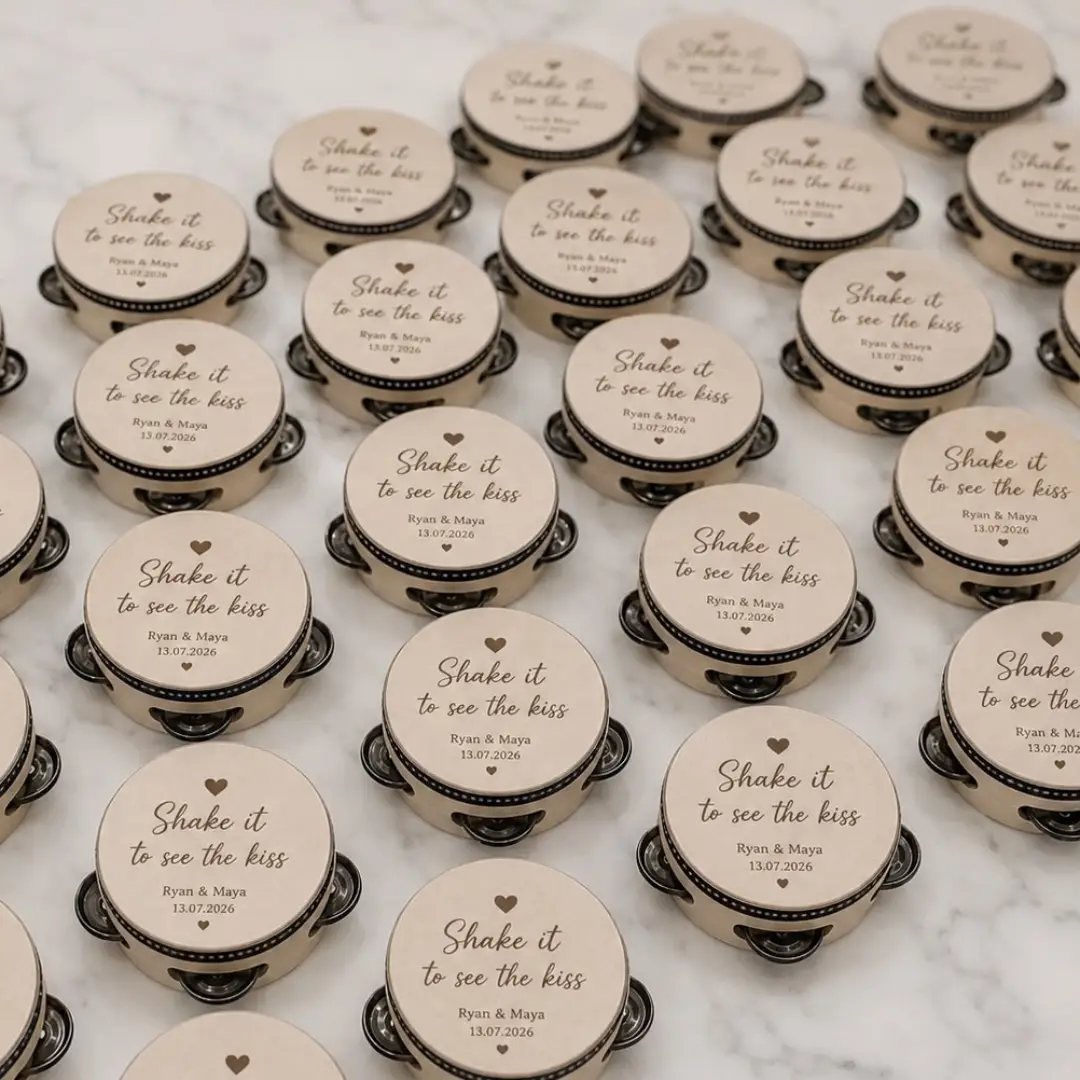 Small cream-colored tambourines with printed wedding text arranged on a white marble surface.