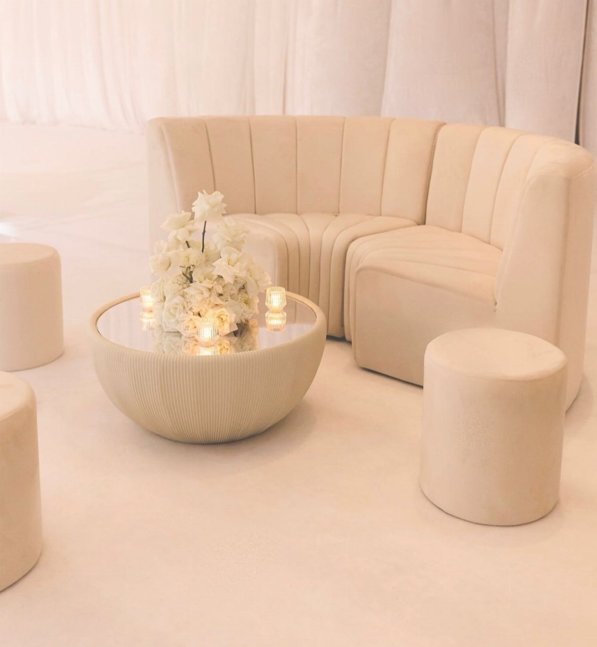 Cream curved sofa and ottomans surrounding a low coffee table with white flowers and candles.