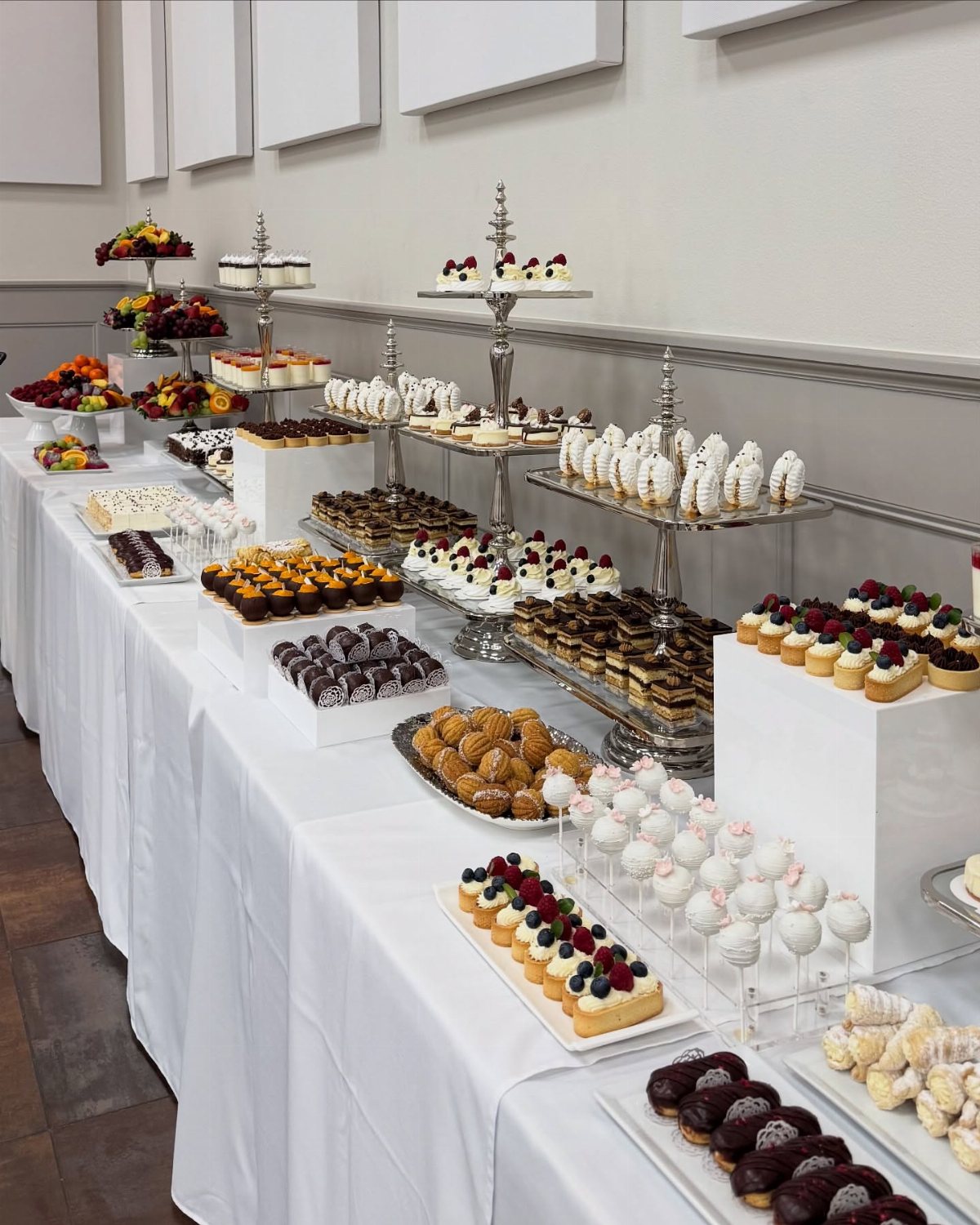 A long white table filled with various gourmet desserts on silver stands and platters.