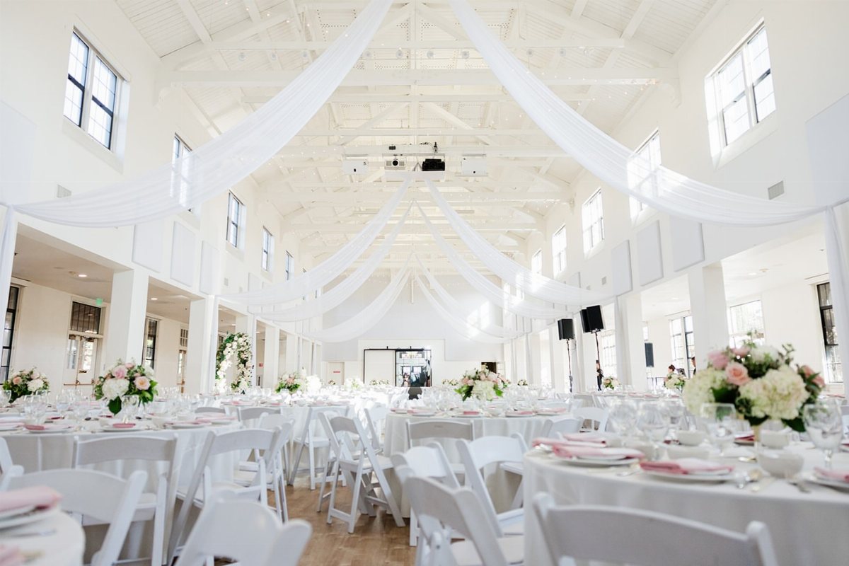 White fabric drapery hangs from the ceiling over wedding reception tables.