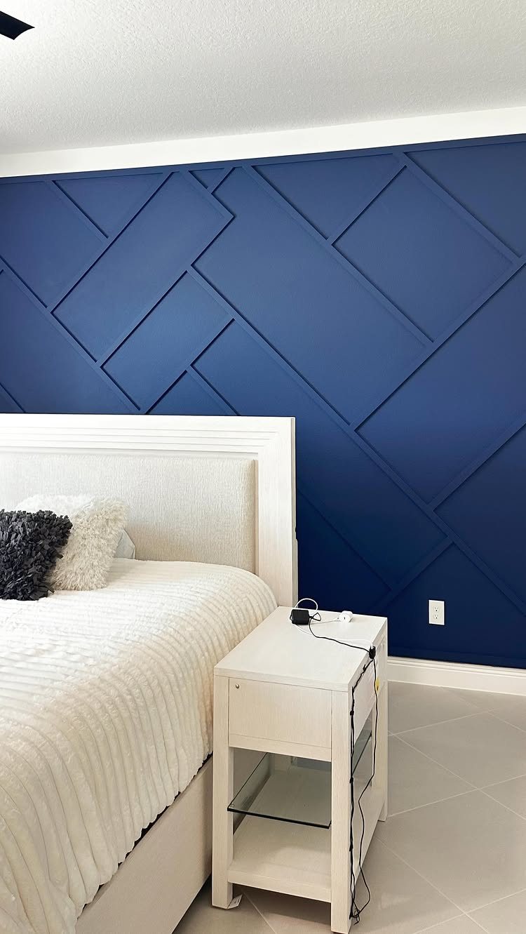 Navy blue geometric patterned accent wall behind a white bed and nightstand.