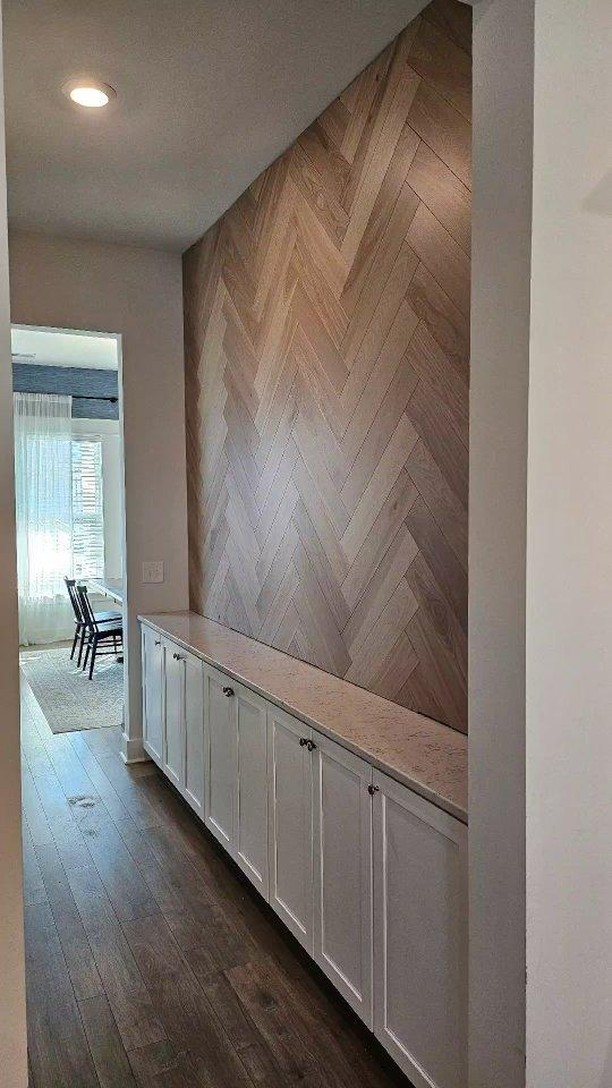 Herringbone pattern wood accent wall above white built-in cabinets in a hallway.