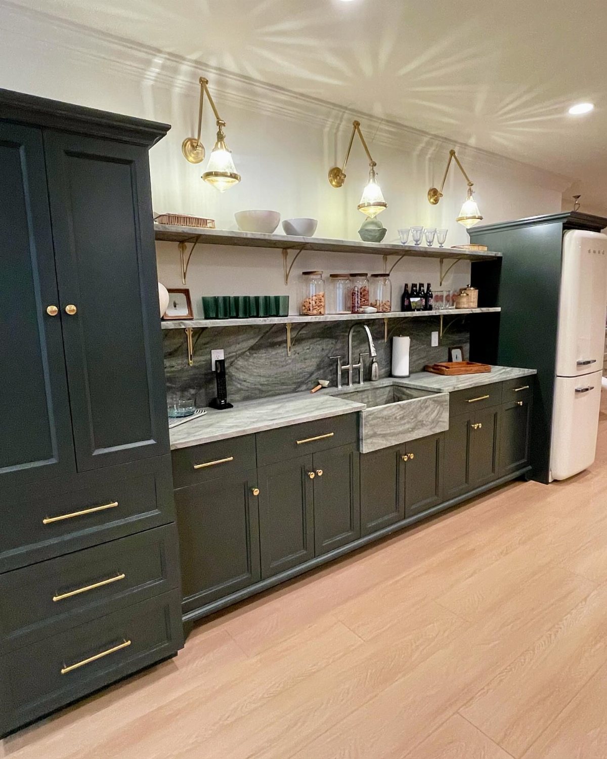 17 Basement Kitchenette Ideas That Maximize Every Square Foot 2 Dark green cabinetry with gold hardware and marble countertops in a modern kitchenette setting.