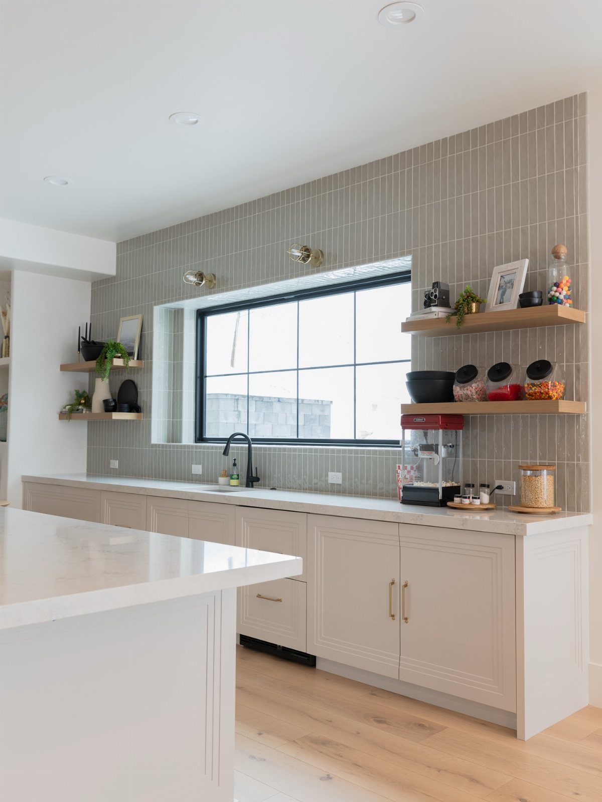 17 Basement Kitchenette Ideas That Maximize Every Square Foot 10 Light beige kitchenette with white countertops, grey tiled backsplash, and a large window providing natural light.