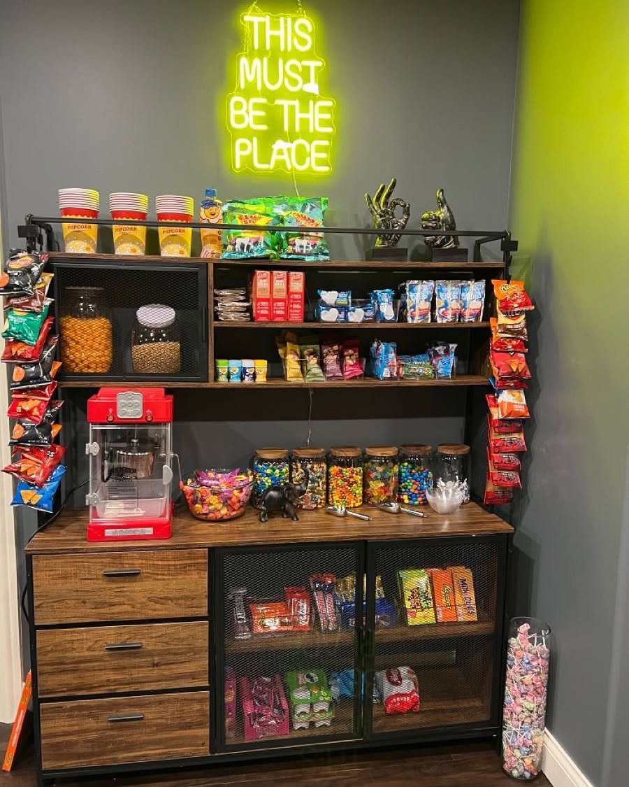 17 Basement Kitchenette Ideas That Maximize Every Square Foot 12 A wooden snack station cabinet filled with candy jars, chips, and a red popcorn machine.
