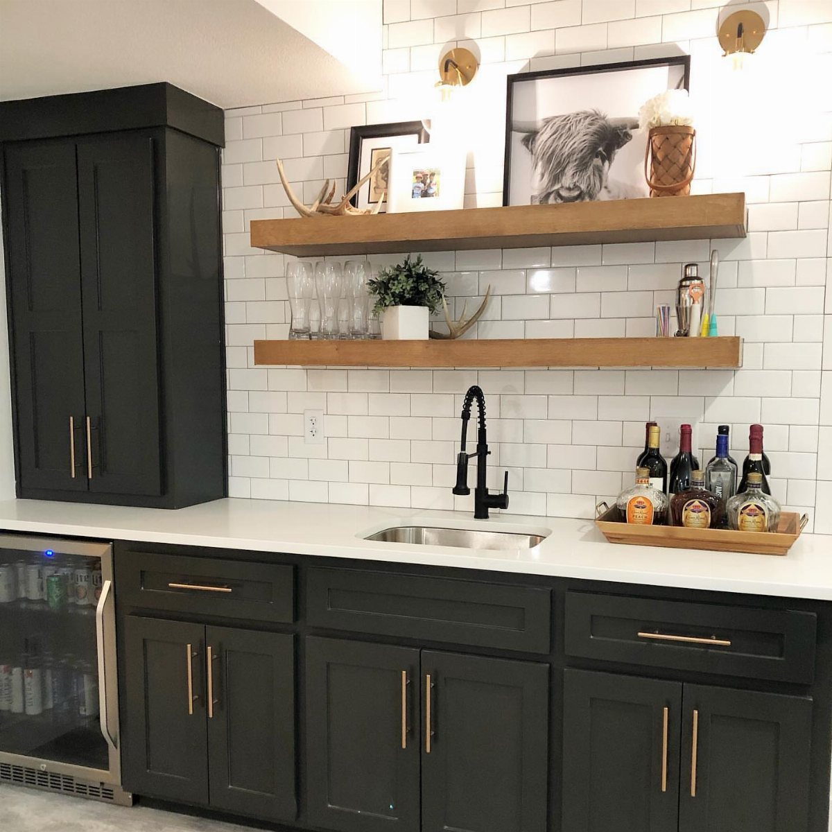 17 Basement Kitchenette Ideas That Maximize Every Square Foot 7 Dark charcoal cabinets with gold hardware and wooden floating shelves against a white subway tile backsplash.