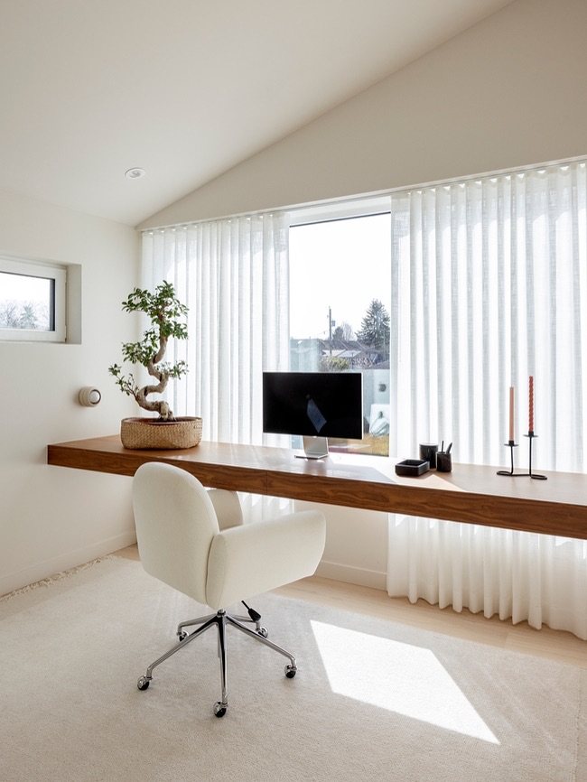 20 Bedroom Office Ideas for Small Spaces and Dual-Purpose Rooms 2 A long wooden floating desk with a white chair and computer monitor in a bright room.