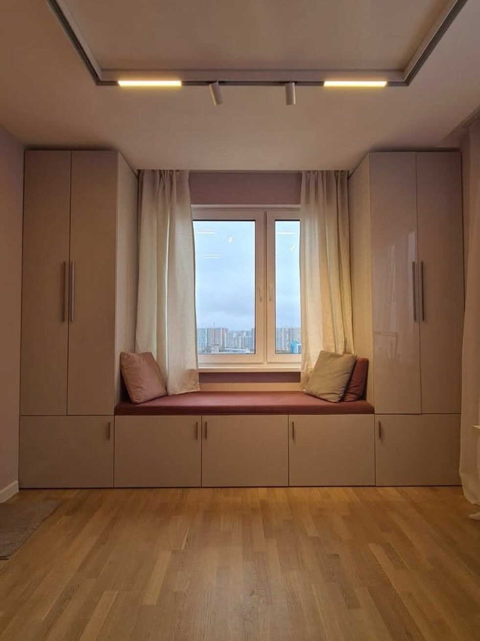 20 Bedroom Office Ideas for Small Spaces and Dual-Purpose Rooms 10 Built-in window seat with maroon cushion and storage cabinets under a bright window.