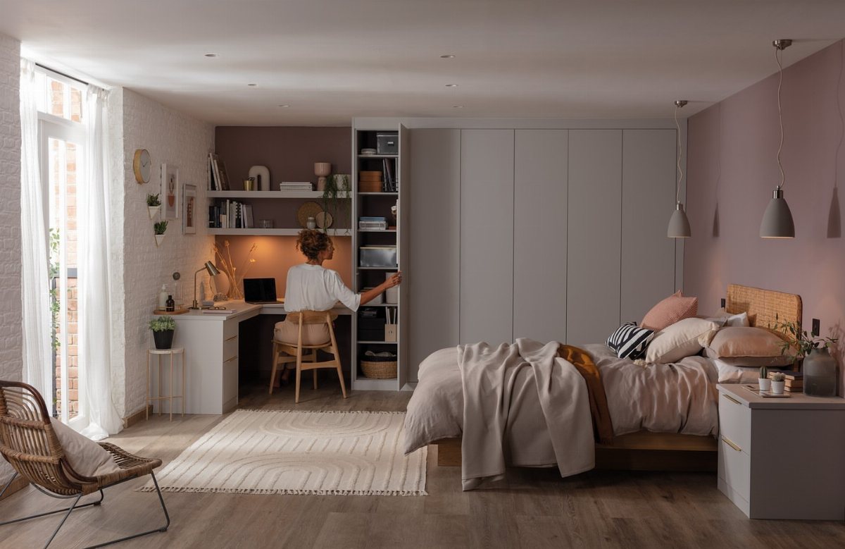 20 Bedroom Office Ideas for Small Spaces and Dual-Purpose Rooms 15 A woman reaches into a tall white shelving unit in a modern bedroom office.