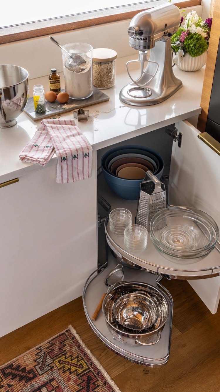 8 Corner Cabinet Ideas for Kitchens That Actually Work 5 Open white corner cabinet with rotating silver shelves holding various glass and metal kitchen bowls.