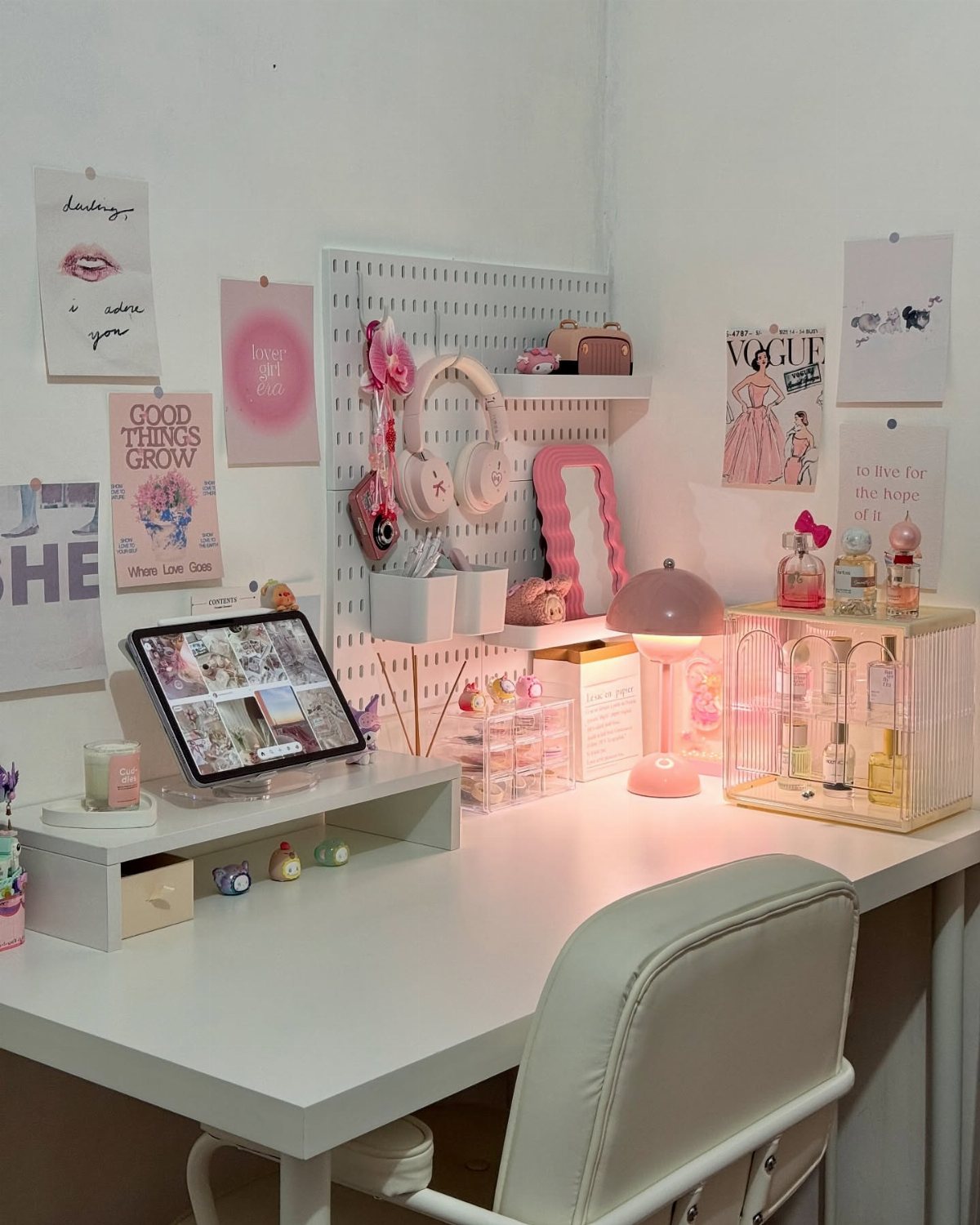 A white desk decorated with various pink aesthetic stationery, accessories, and posters on a white wall.