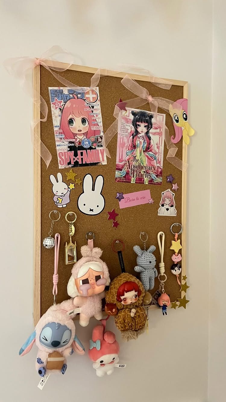 A cork pinboard decorated with anime prints, stickers, and various hanging plush keychains.