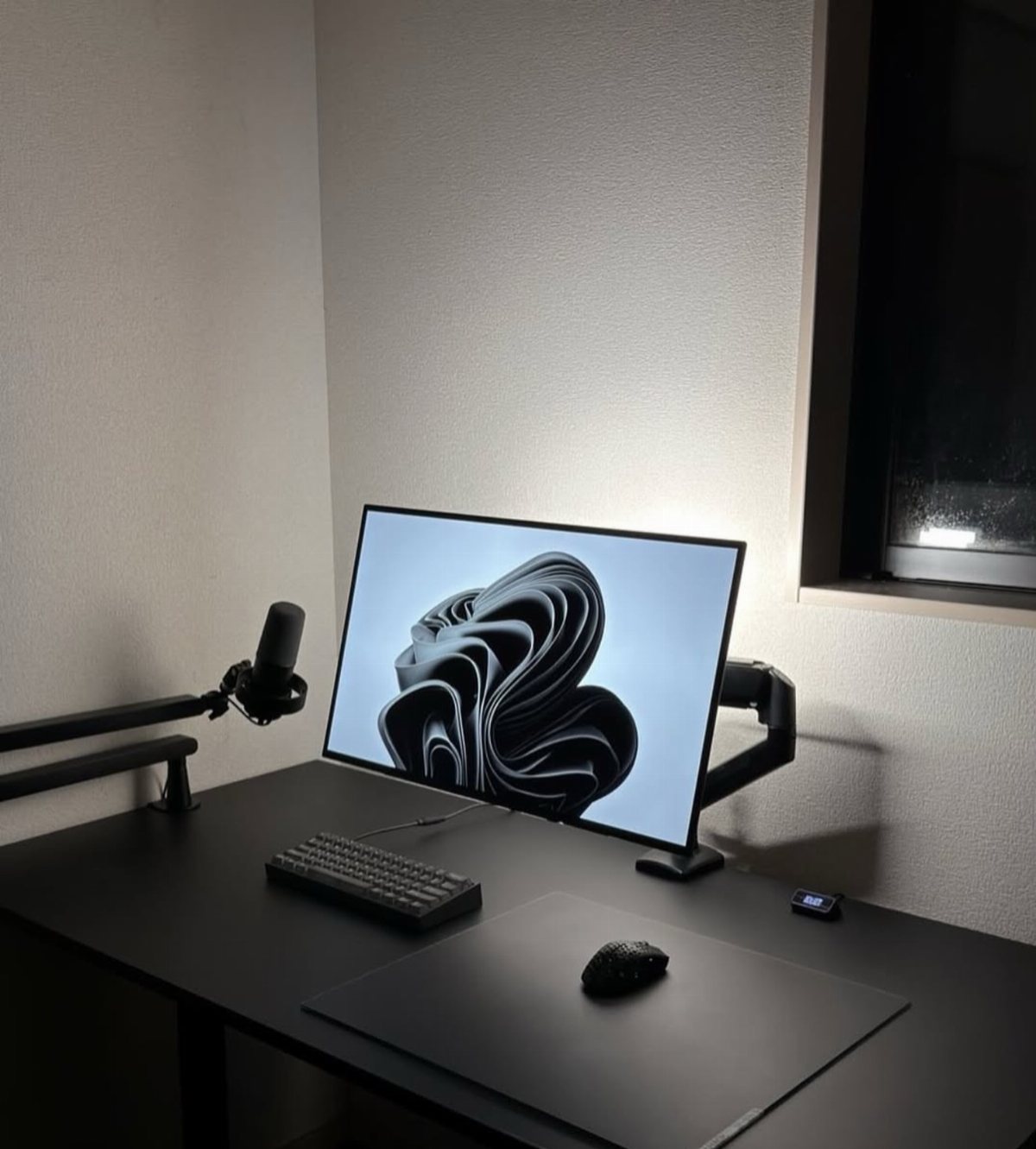 11 Desk Organization Ideas That Tidy Your Space for 2026 6 Minimalist black desk setup with a monitor, keyboard, mouse, and microphone arm in a dark room.