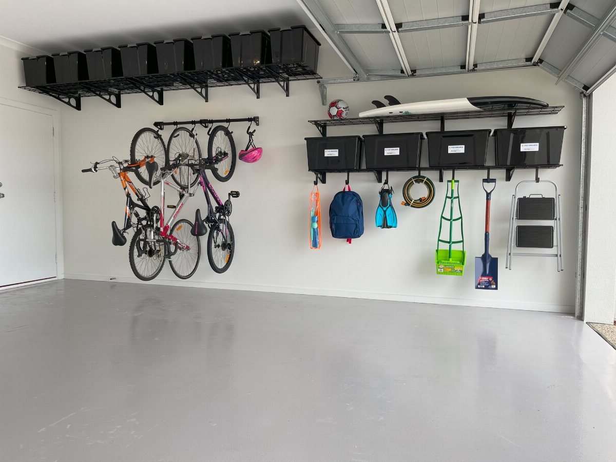 Bicycles hanging vertically on black wall hooks in a clean, organized white garage.