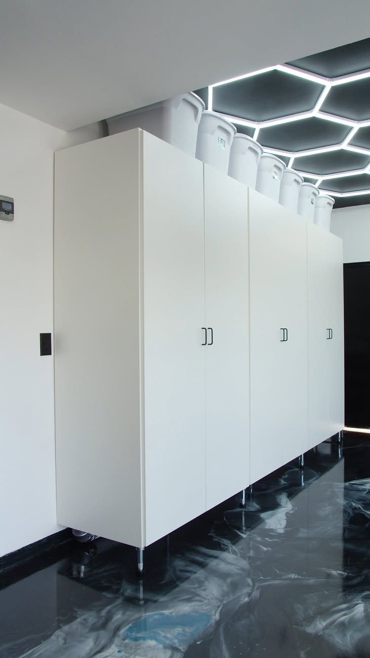 Tall white custom cabinets standing on a polished black epoxy garage floor under hexagonal lights.