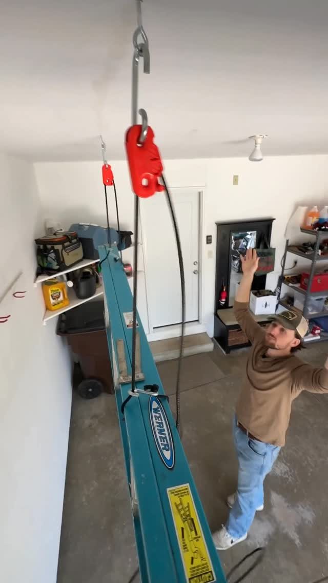 A man reaches toward a teal ladder being lifted to the ceiling by a red pulley system.