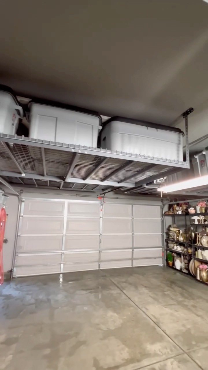 Metal overhead storage rack mounted to a garage ceiling holding large white plastic bins.