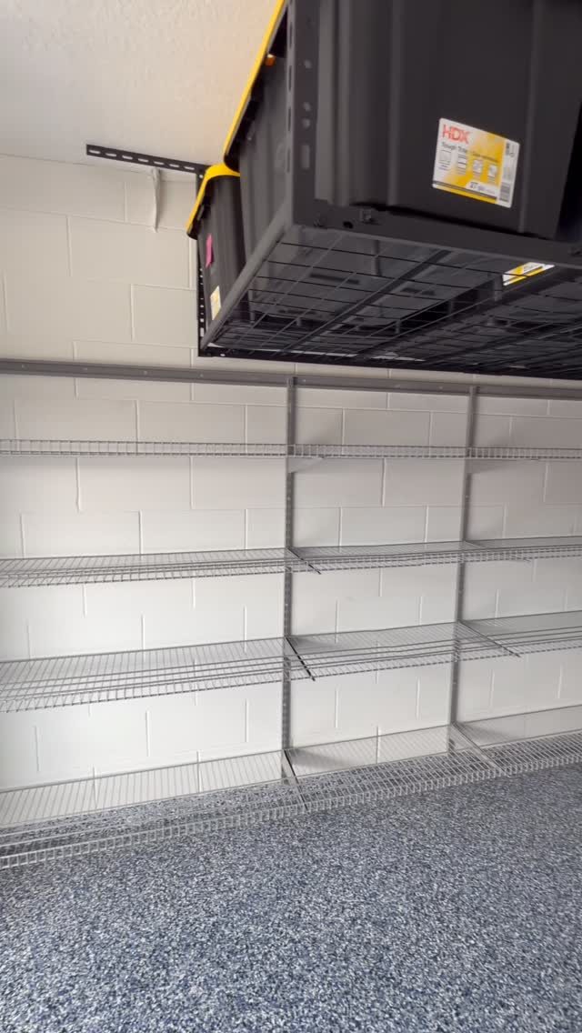 Empty metal wire shelving units installed against a white cinder block wall in a garage.