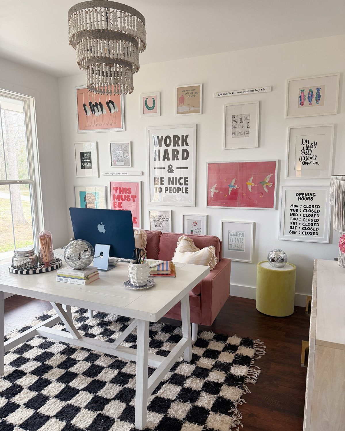 A white desk and pink sofa sit below a large gallery wall of framed art.
