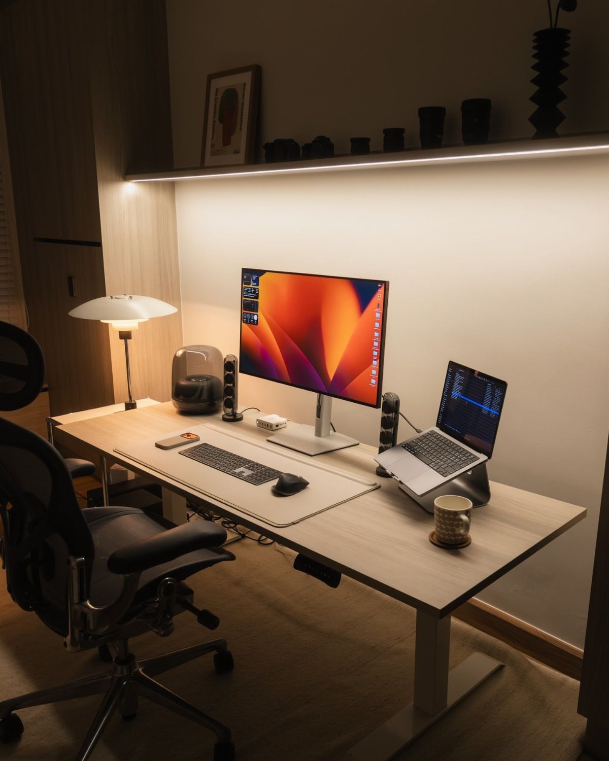 A sleek wooden desk setup with a large monitor, laptop, and ergonomic chair in a home office.