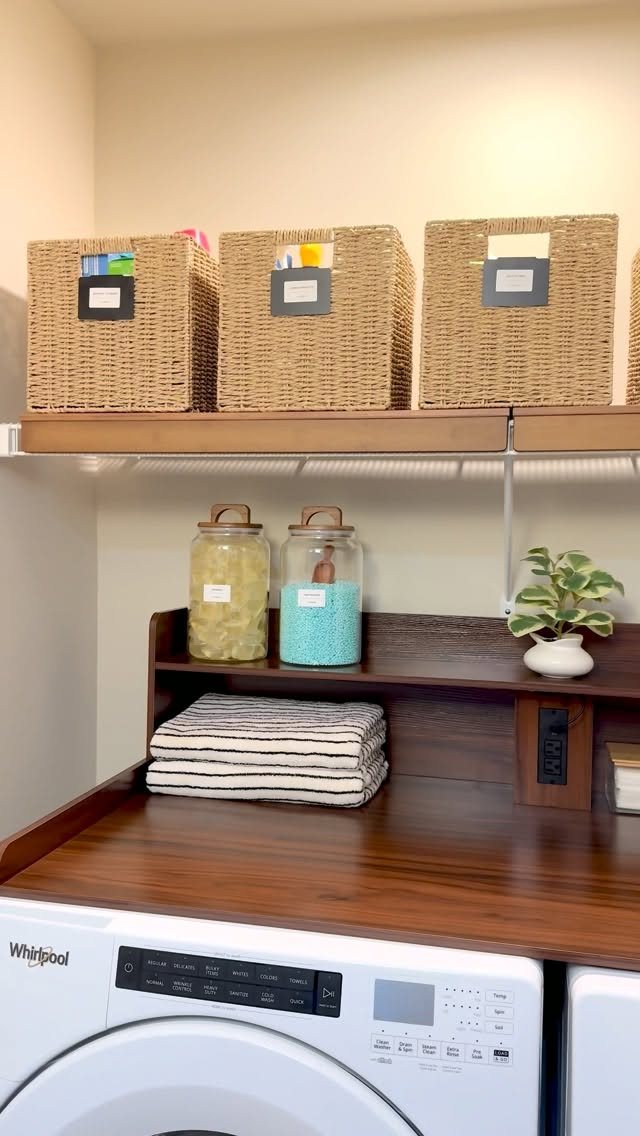 17 Laundry Room Ideas for Storage, Style and Smarter Layouts 2 Wooden countertop with folded towels, glass jars, and a small plant above white washing machines.