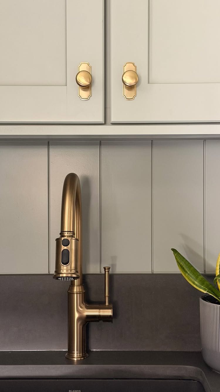 17 Laundry Room Ideas for Storage, Style and Smarter Layouts 15 Gold cabinet knobs on light grey cabinets above a gold faucet and dark countertop.