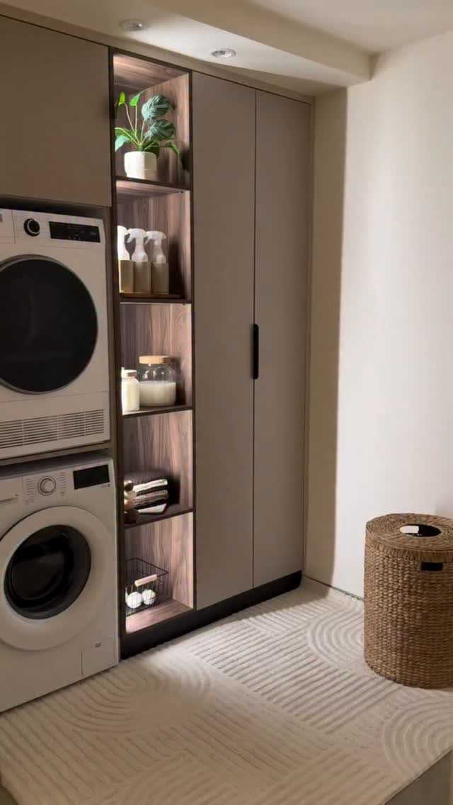 17 Laundry Room Ideas for Storage, Style and Smarter Layouts 4 Tall taupe laundry cabinets with integrated illuminated shelving displaying plants and bottles next to a washer and dryer.