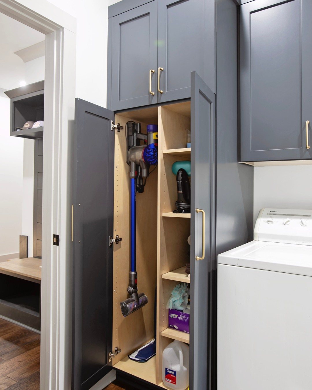 17 Laundry Room Ideas for Storage, Style and Smarter Layouts 8 Tall grey laundry cabinet with open door showing vacuum and cleaning supplies stored vertically.