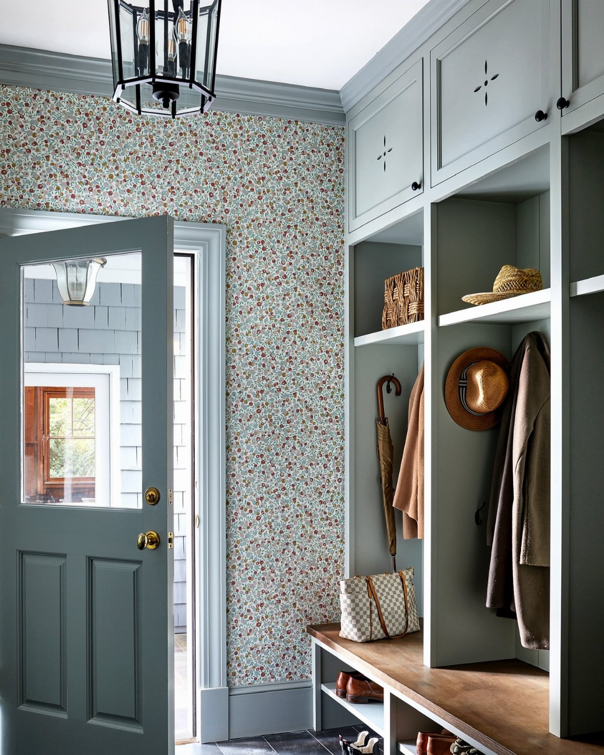 17 Mudroom Ideas for Entryways That Actually Work in 2026 7 Floral patterned wallpaper on a mudroom wall next to light blue built-in storage cubbies.