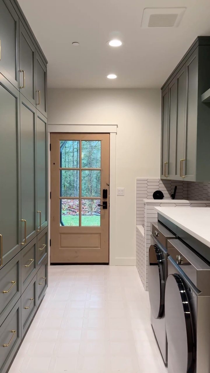 17 Mudroom Ideas for Entryways That Actually Work in 2026 11 Grey built-in cabinets and laundry machines line a narrow utility room with a glass door.