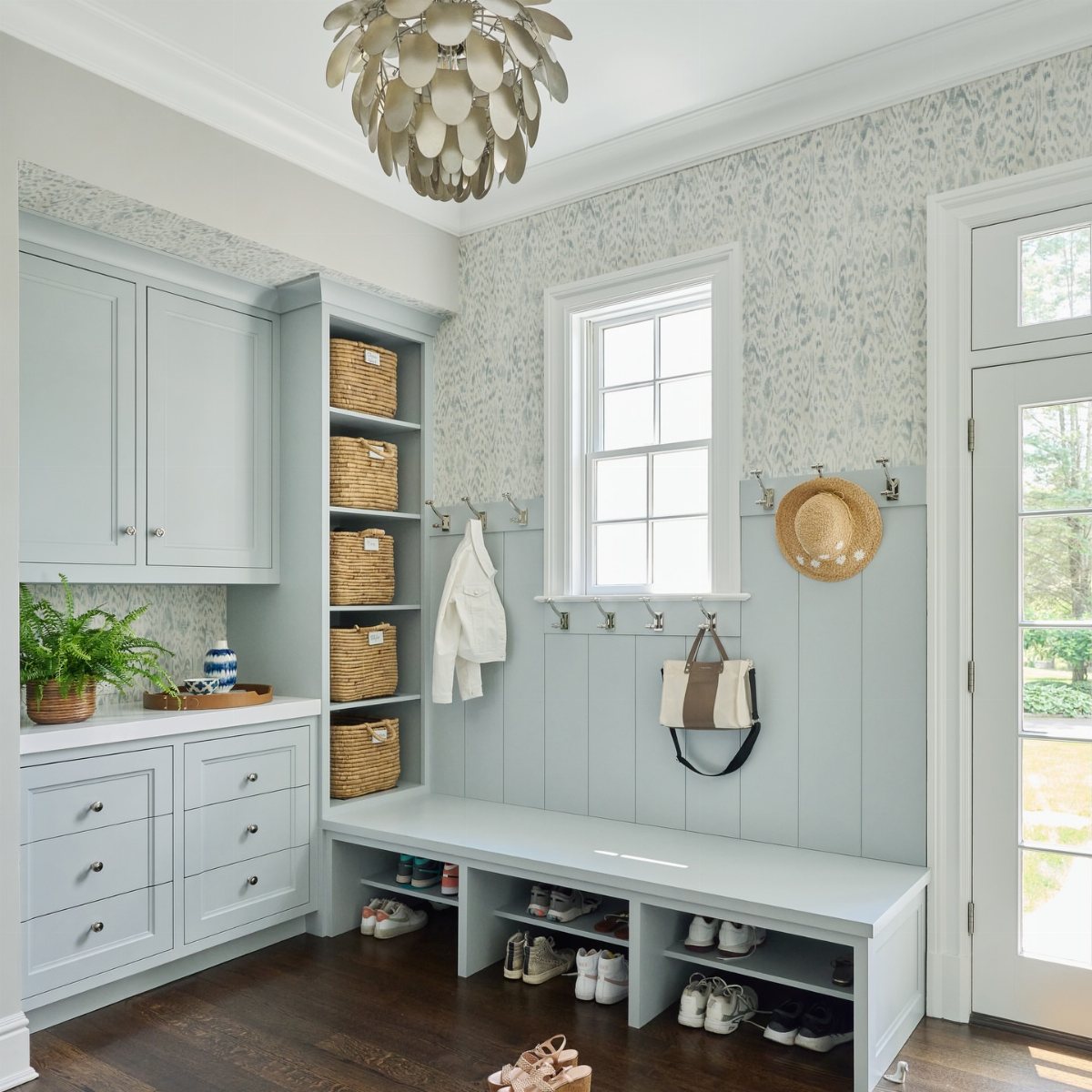 17 Mudroom Ideas for Entryways That Actually Work in 2026 12 A light blue mudroom with built-in storage, a bench, and a large metallic pendant light.