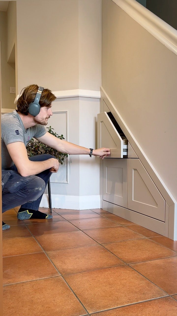 17 Mudroom Ideas for Entryways That Actually Work in 2026 9 A man opens a built-in storage cabinet located under a staircase on a tiled floor.