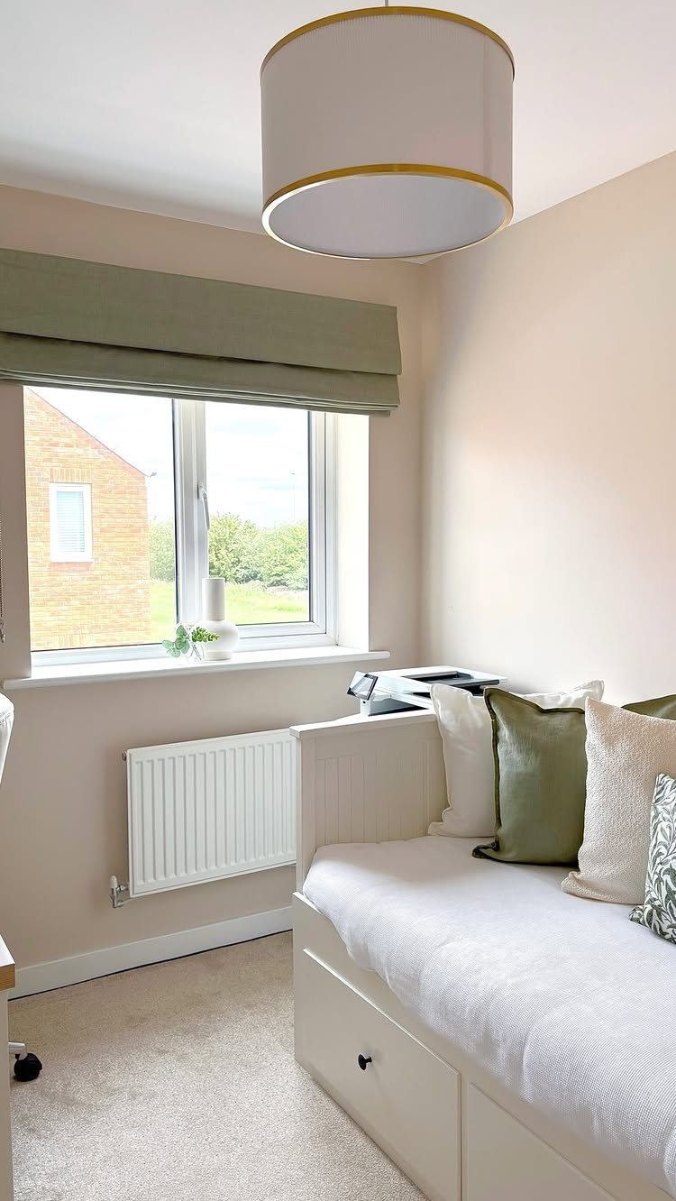 White daybed with storage drawers and green pillows positioned next to a bright window.