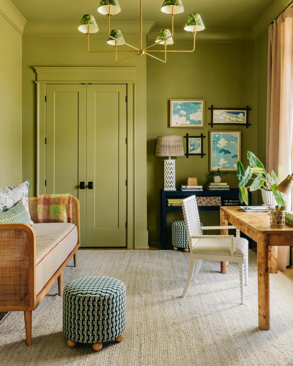 Green room with wooden desk, white chair, patterned ottoman, and framed wall art.
