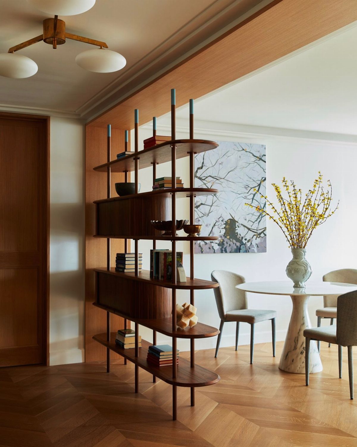 A dark wood open-shelf bookcase serving as a room divider in a modern dining room.