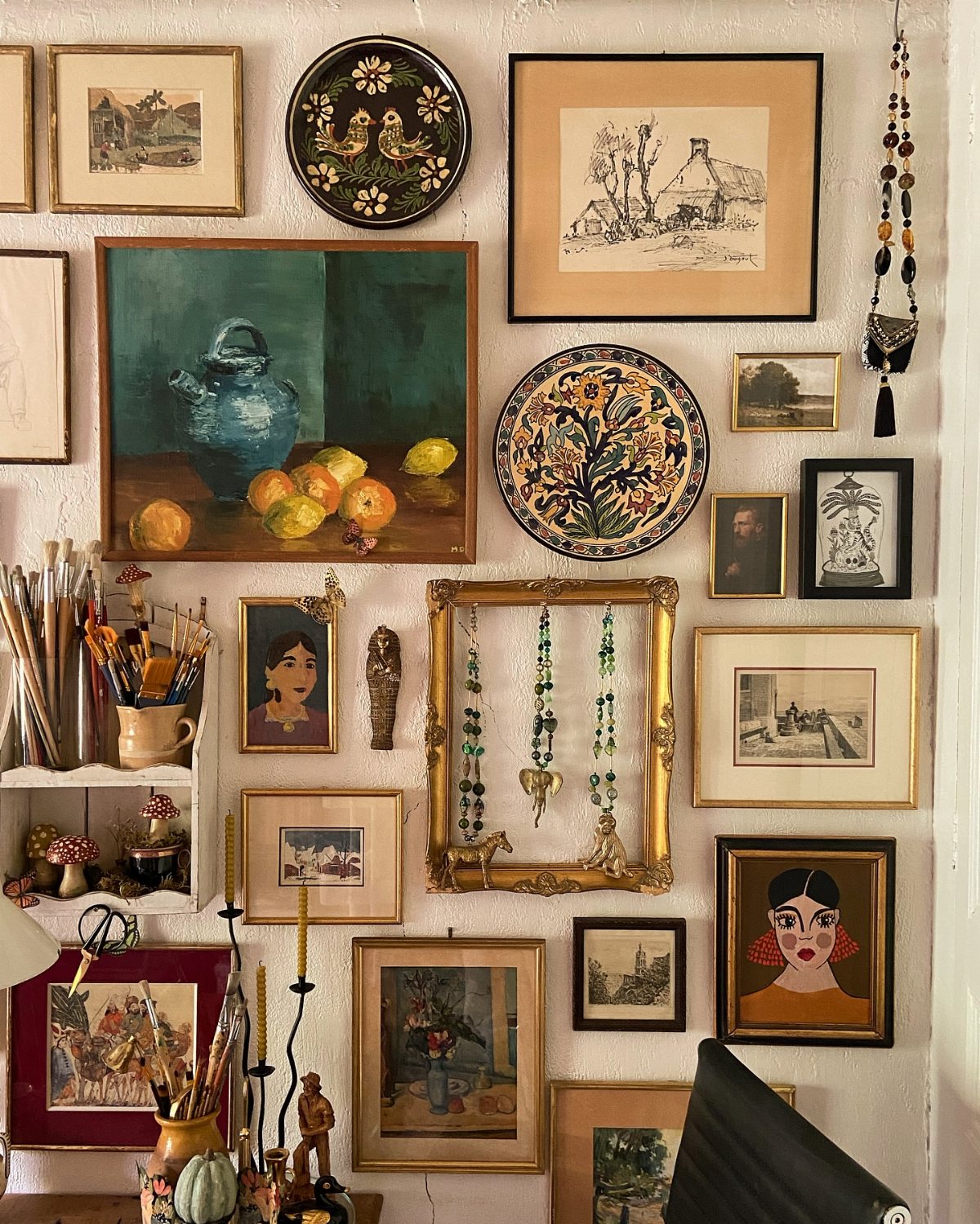 A collection of framed art pieces, decorative plates, and jewelry arranged on a white wall.