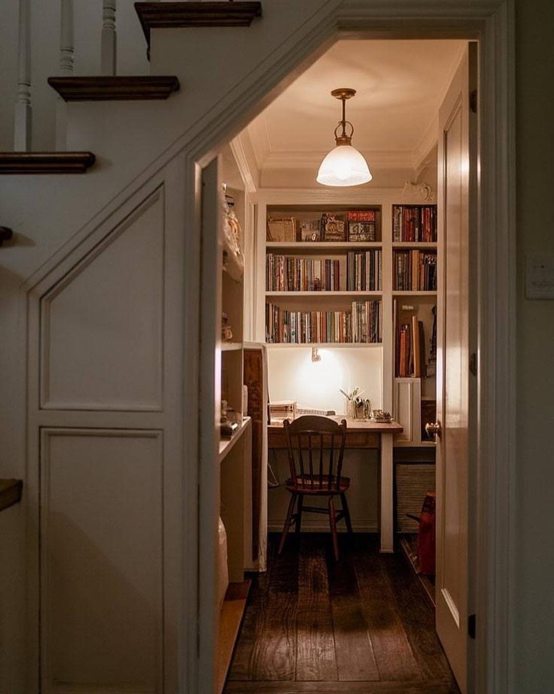 A small wooden desk and bookshelves tucked into a cozy nook under a staircase.