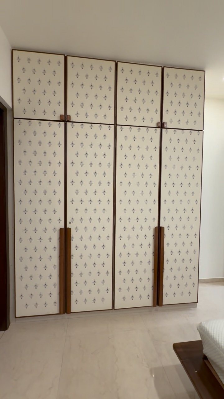 Large white wardrobe with patterned doors and wooden handles in a bright room.