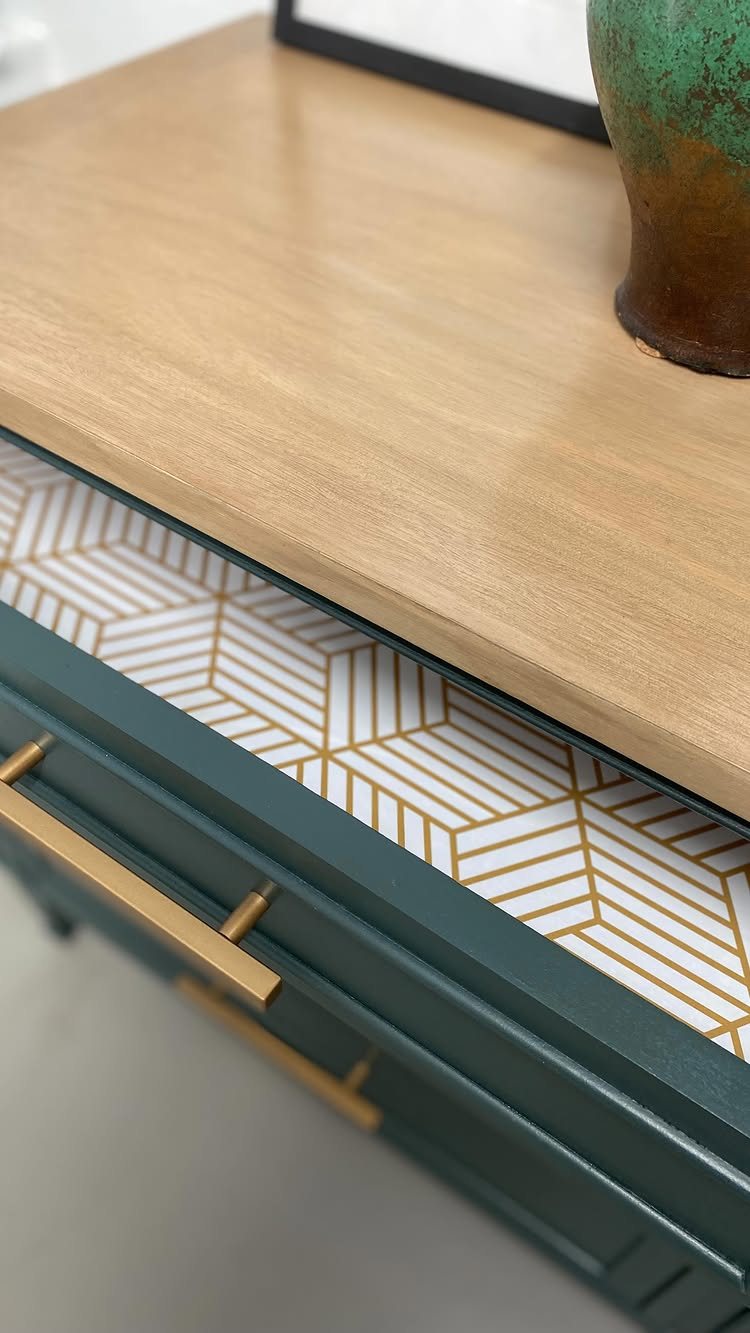 Teal dresser with an open drawer lined in gold geometric patterned wallpaper.