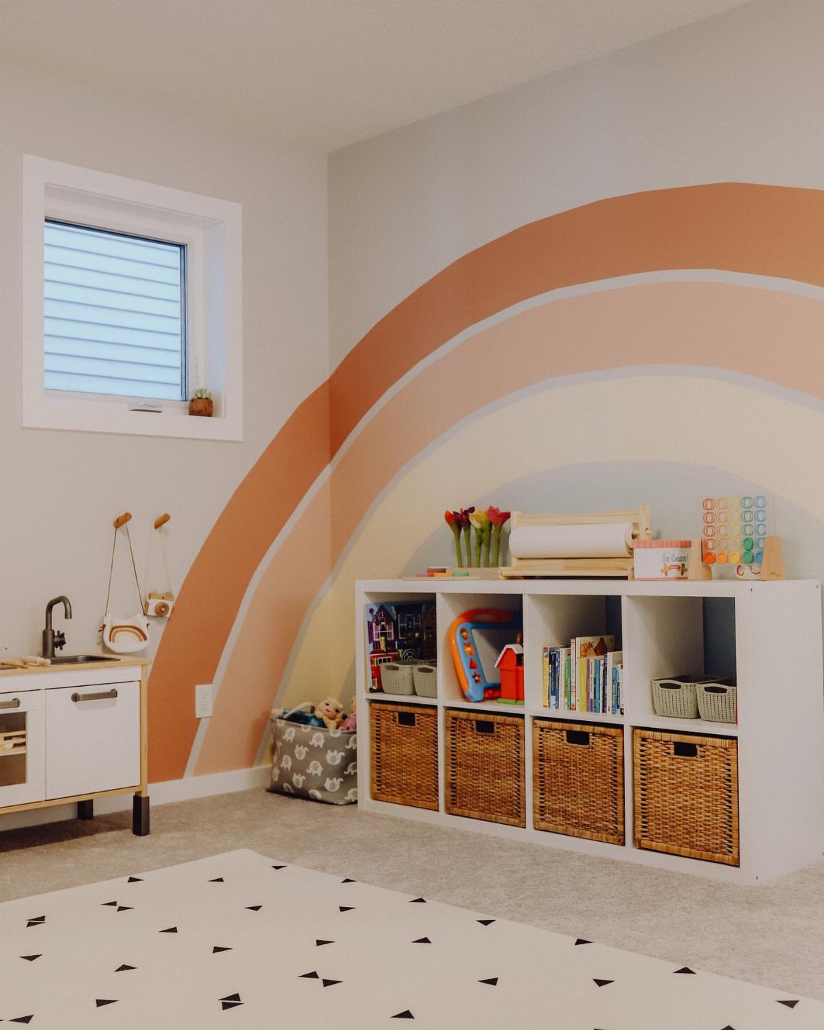 A playroom wall featuring a large painted rainbow mural above white storage cubbies with wicker baskets.