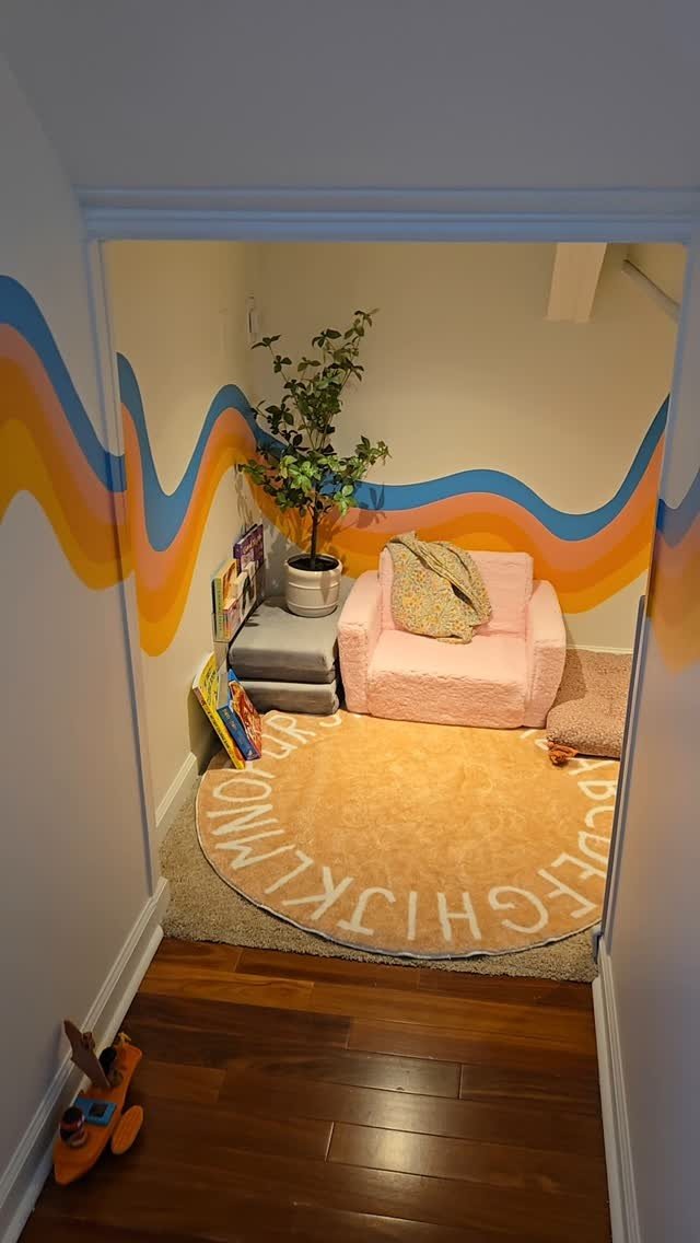 A cozy reading nook with a pink armchair, alphabet rug, and wavy patterned walls.