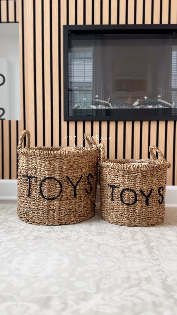 Two woven seagrass baskets with the word TOYS printed on them sit on a rug.