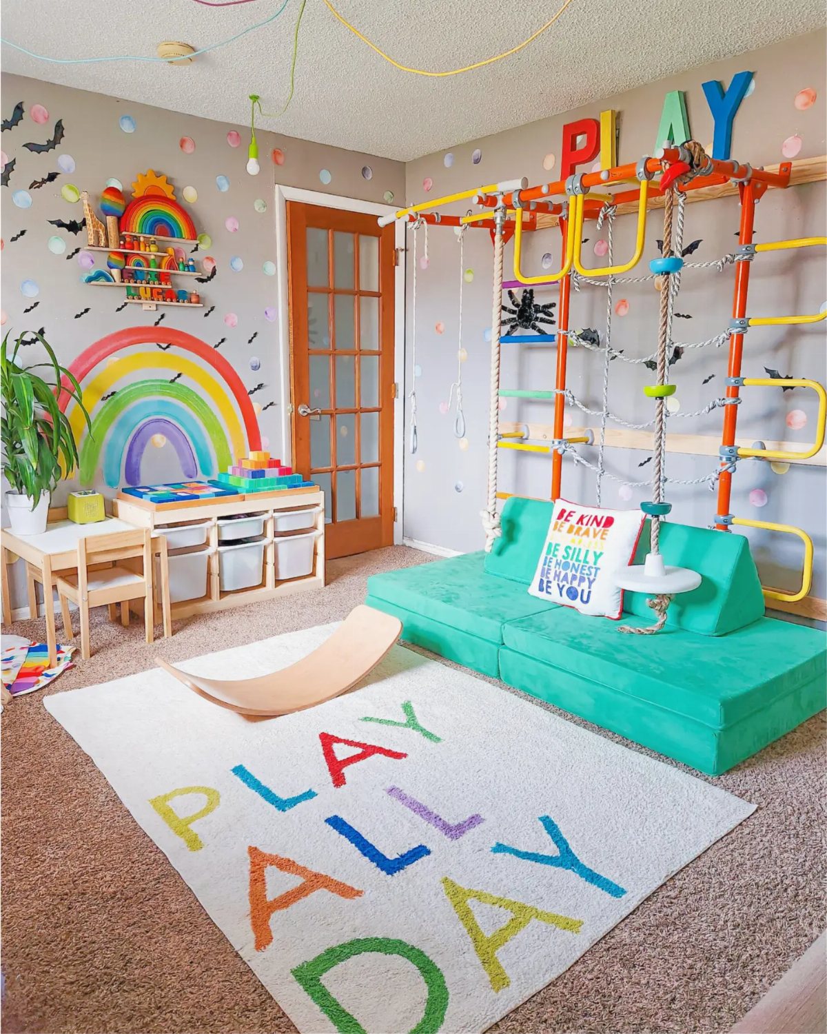 Colorful playroom with rainbow wall art, teal modular sofa, and a climbing gym structure.
