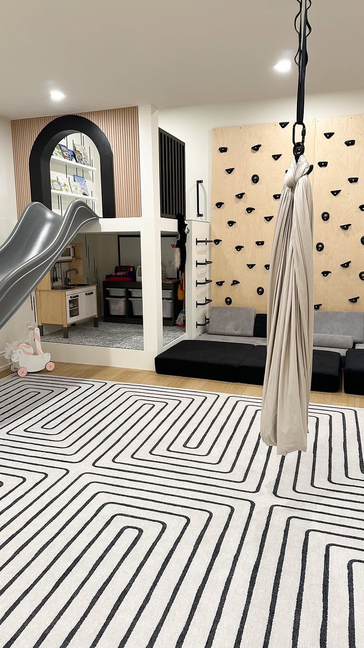 Children's playroom with a climbing wall, slide, play kitchen, and geometric rug.