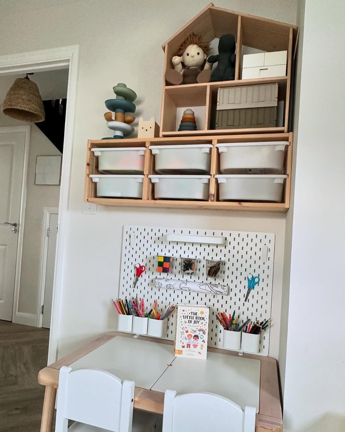 White pegboard holding art supplies mounted on a wall above a small child's table.