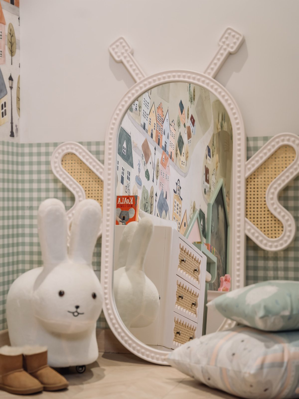 Oval white butterfly-shaped mirror reflecting a playroom with a bunny chair and patterned wallpaper.