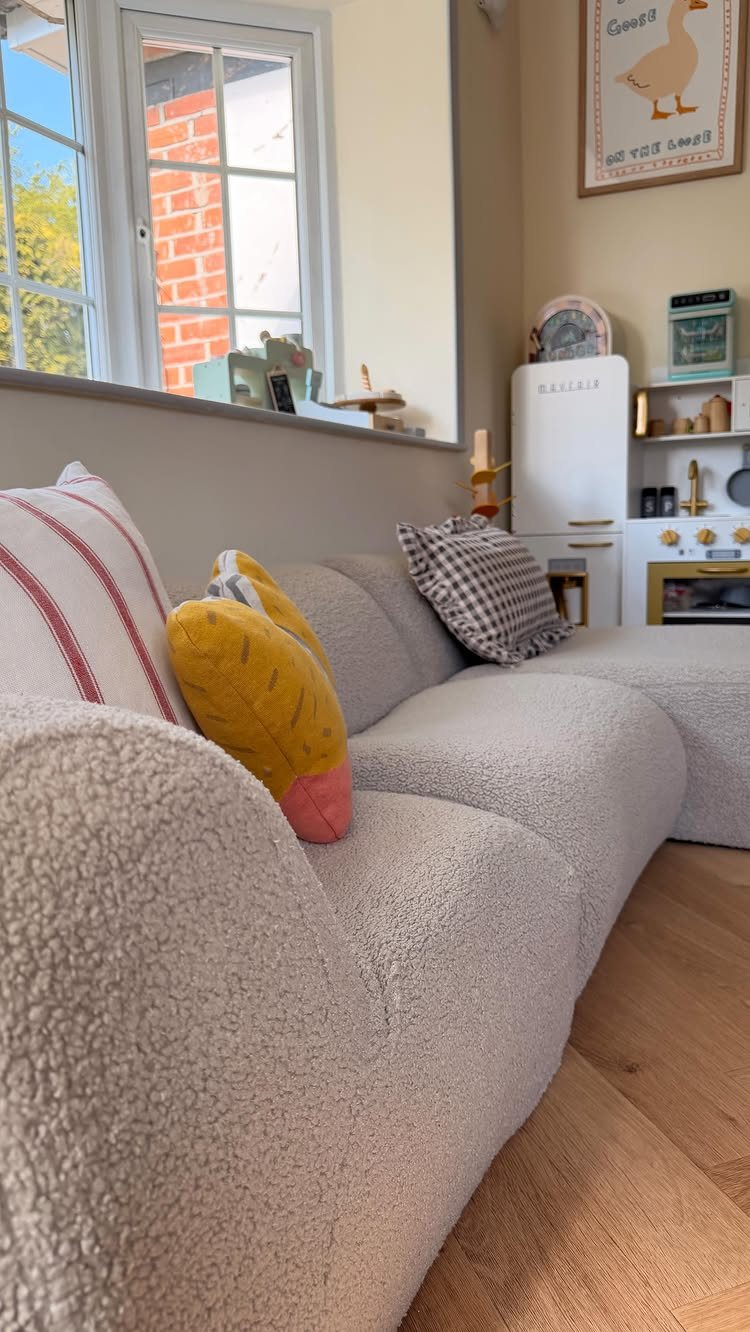 10 Ideas for Small Playroom Inspiration: Layout to Decor 6 Cream bouclé sofa with colorful pillows in a bright room with a play kitchen.