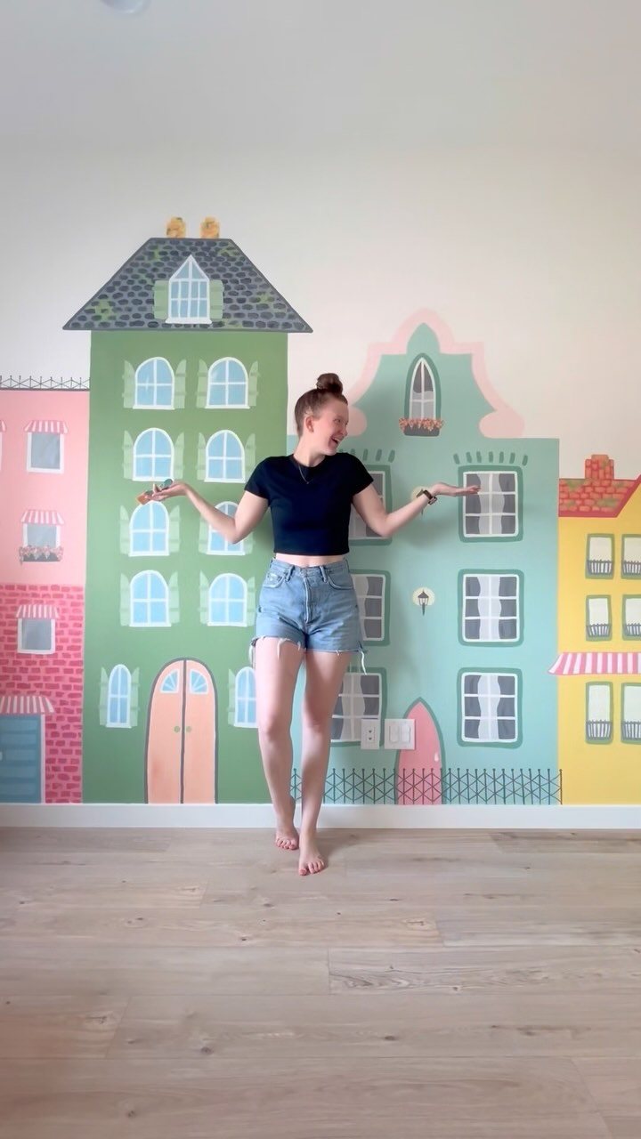 10 Ideas for Small Playroom Inspiration: Layout to Decor 5 A woman posing in front of a colorful townhouse wall mural in a room.
