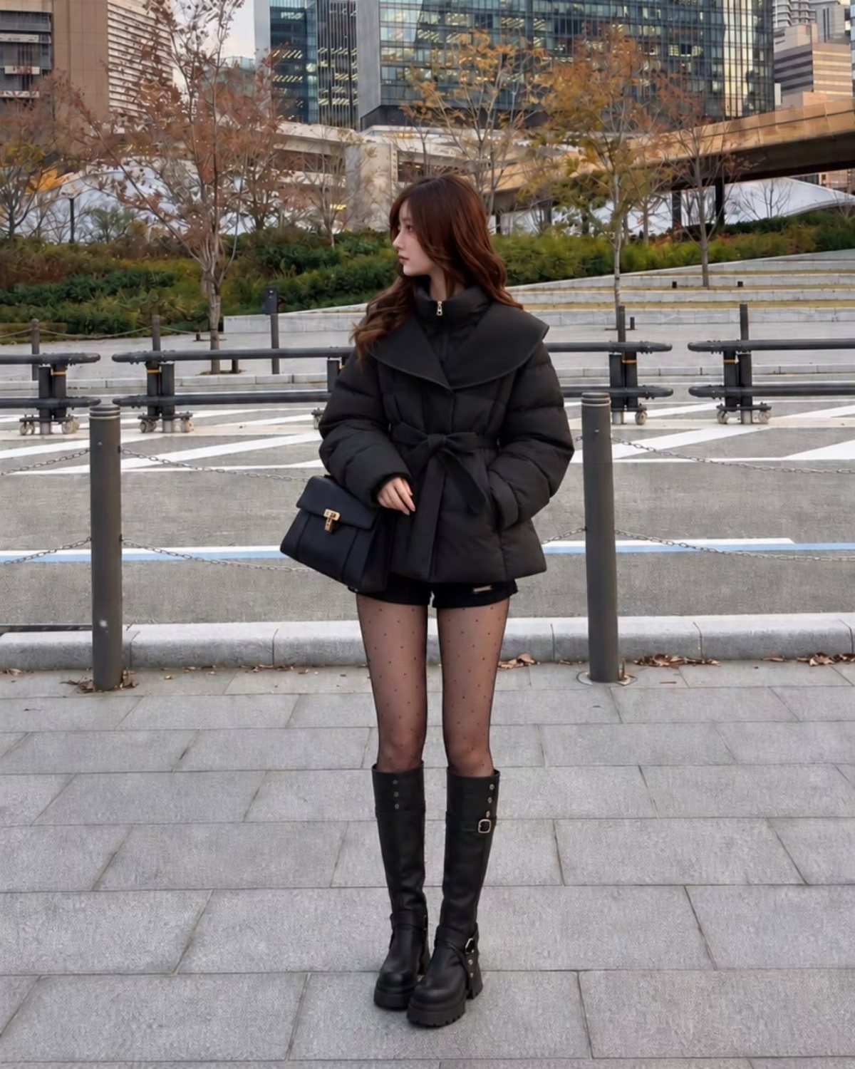 Woman wearing a black belted puffer coat, black shorts, sheer tights, and platform boots.